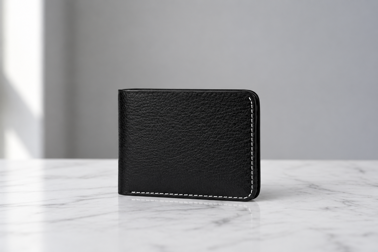 A black textured leather bifold wallet with white contrast stitching, standing upright on a white marble surface against a light gray background.