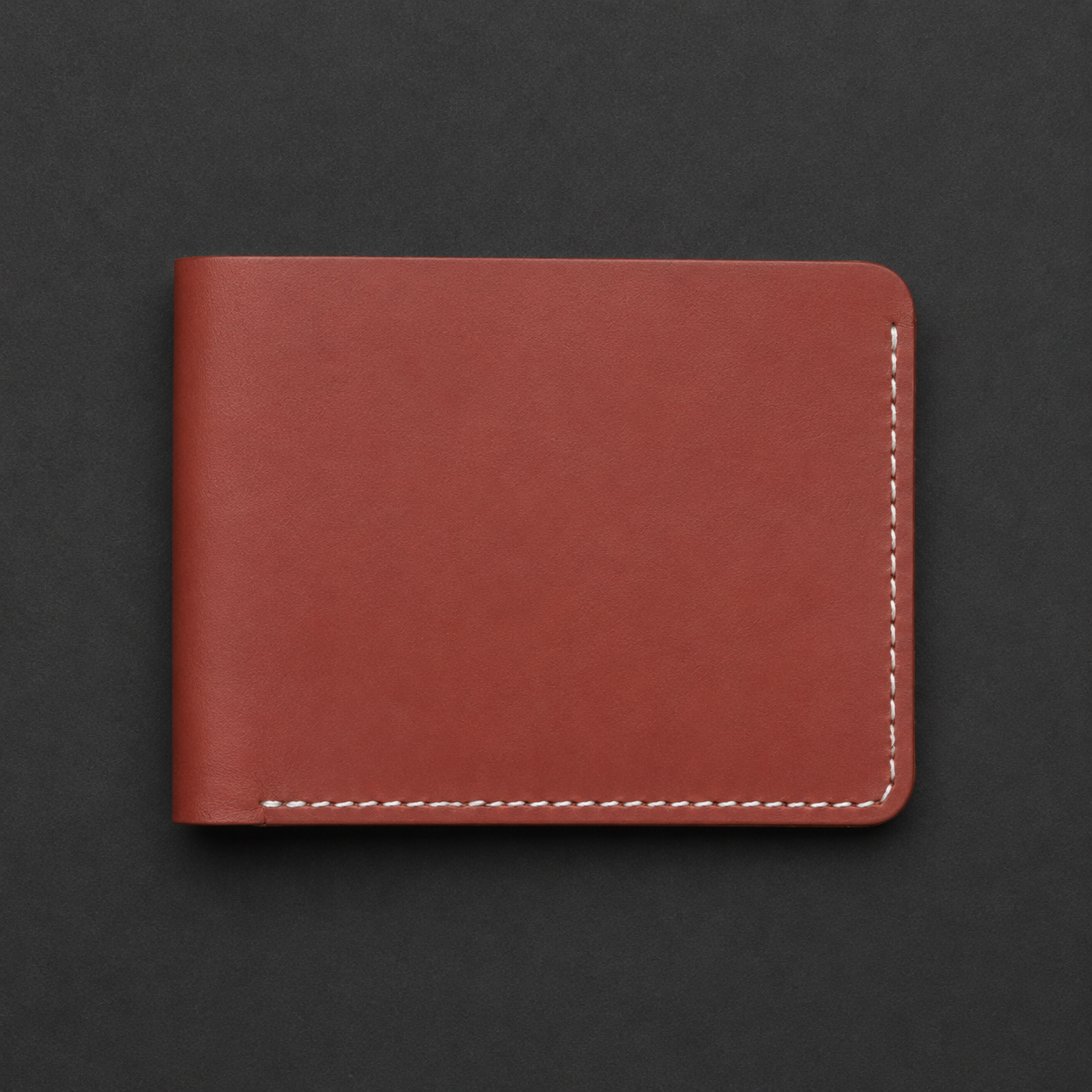 A minimalist reddish-brown leather wallet with white contrast stitching, shown closed on a dark textured background.