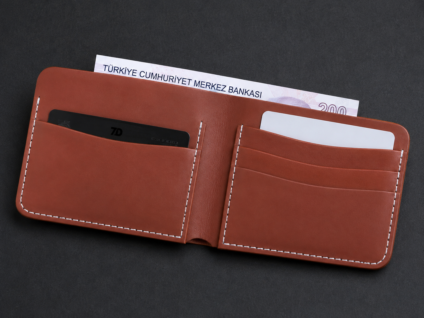 A brown leather wallet shown open on a dark gray background, with card slots, white contrast stitching, and banknotes partially visible inside.