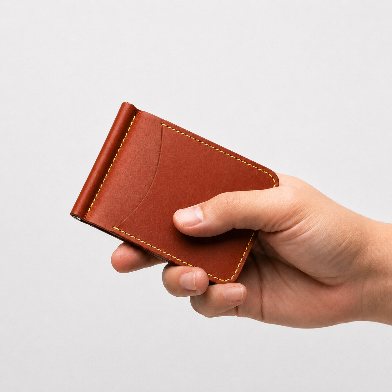 A hand holding a small brown leather card holder or wallet with visible contrast stitching, shown against a plain light gray background.